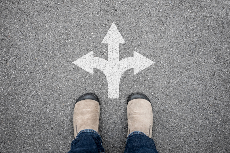 Staring down at feet standing above arrows pointing left, right and straight ahead