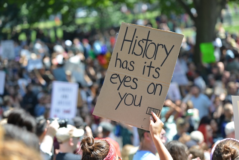 View of a protest with a prominent sign that reads "History has its eyes on you"