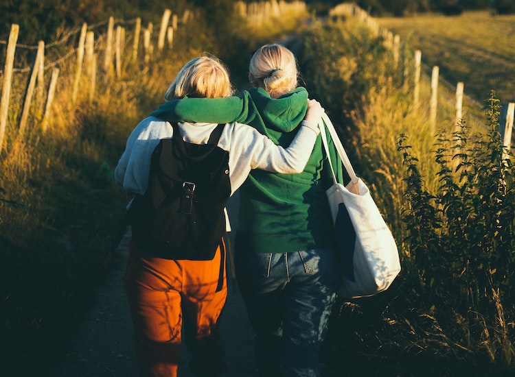 Two friends walking away from the camera, hugging one another close