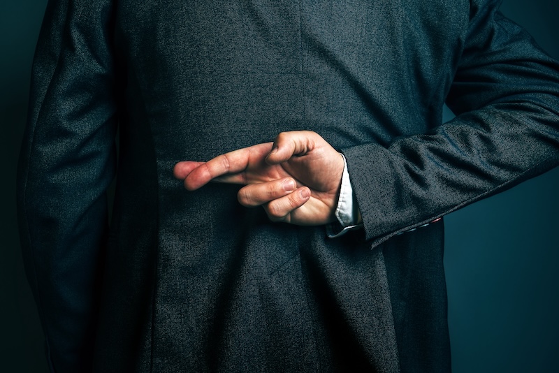 A suit-clad person with their fingers crossed behind their back